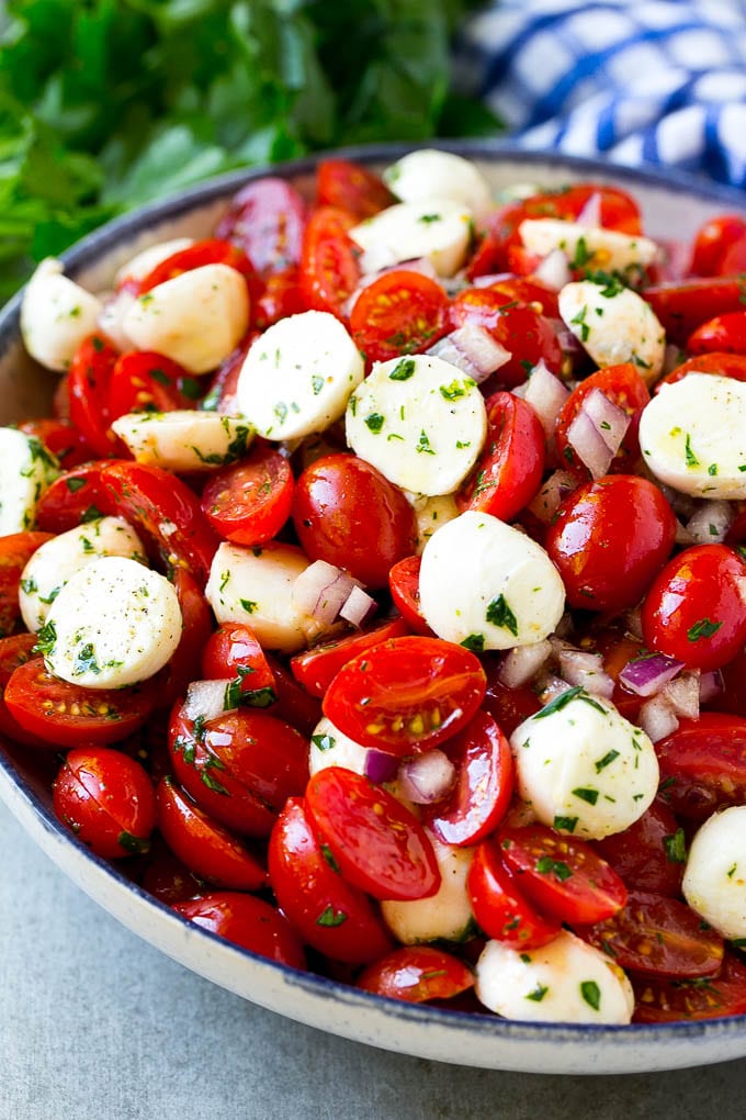 Cherry tomato salad with halved cherry tomatoes, mozzarella balls and red onion, all tossed with herbs and dressing.