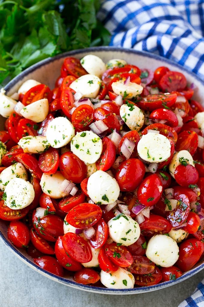 A serving bowl of tomato mozzarella salad with cherry tomatoes, herbs and red onion.