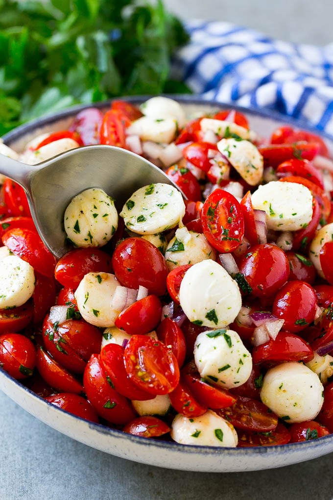 A bowl of cherry tomato salad with a serving spoon in it.