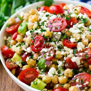 A bowl of chickpea salad with tomatoes, cucumber, avocado, feta cheese and herbs.
