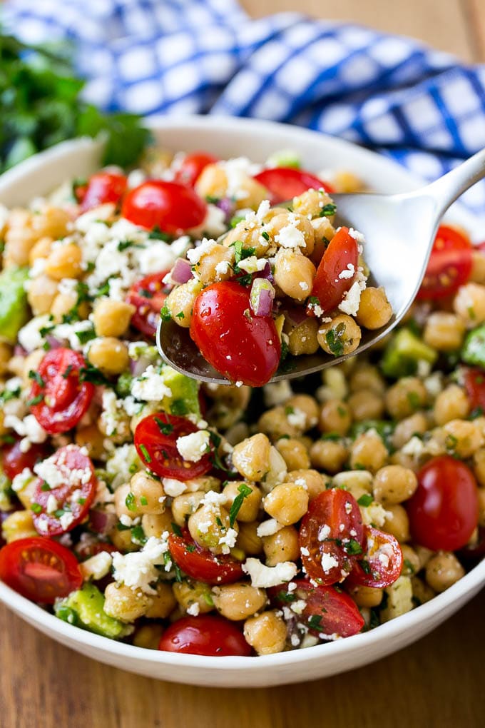 A bowl of chickpea salad with a serving spoon.