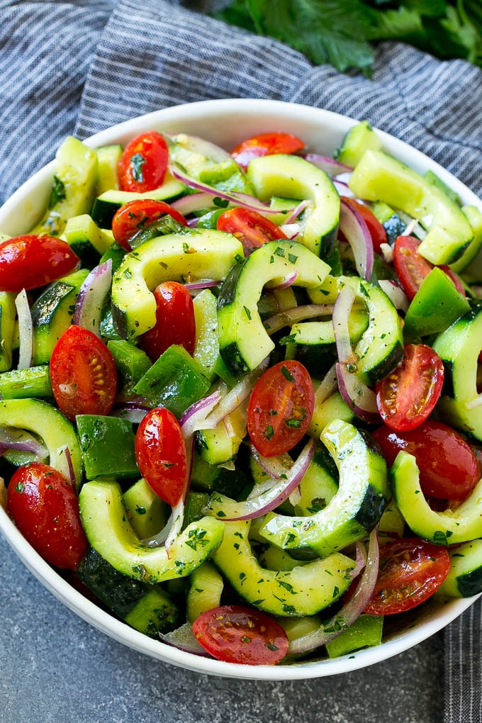 A serving bowl of cucumber tomato salad topping with herb dressing and parsley.