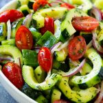 A bowl of cucumber tomato salad with sliced cucumber, cherry tomatoes and red onion, all tossed in vinaigrette.
