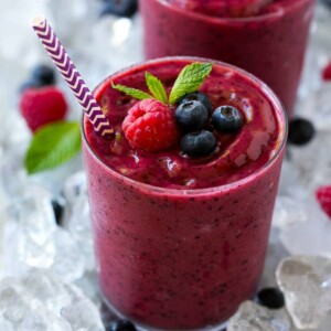 A glass of frozen fruit smoothie in crushed ice, garnished with berries and mint.