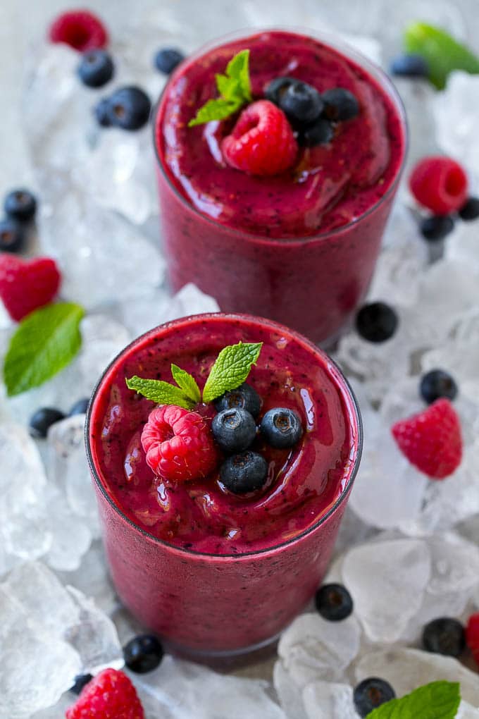Frozen fruit smoothies on a bed of ice with blueberries and raspberries.