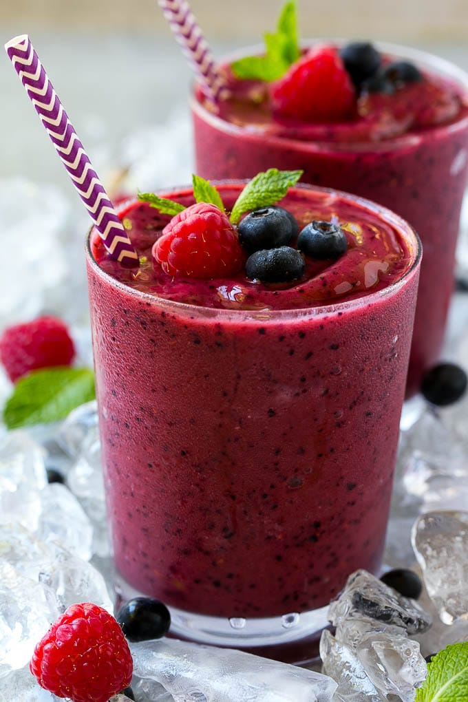 A glass of frozen fruit smoothie with a straw, topped with raspberries, blueberries and mint.
