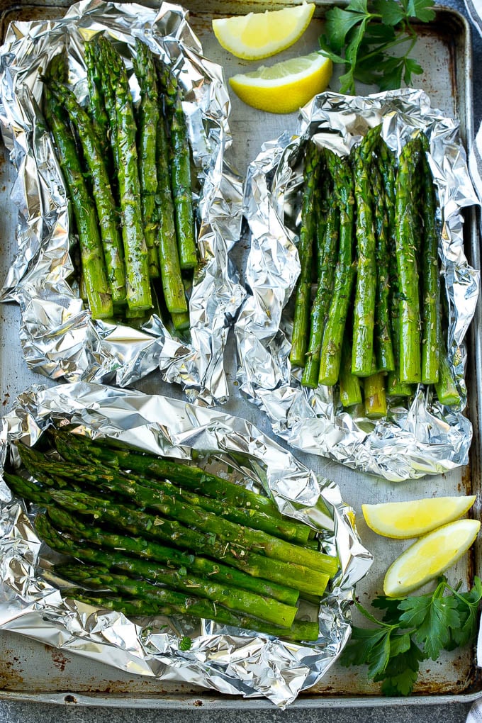 Grilled asparagus in foil on a sheet pan with lemon wedges and parsley.