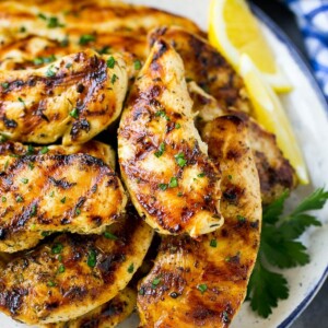 A pile of grilled chicken tenders topped with fresh herbs and garnished with lemon wedges.
