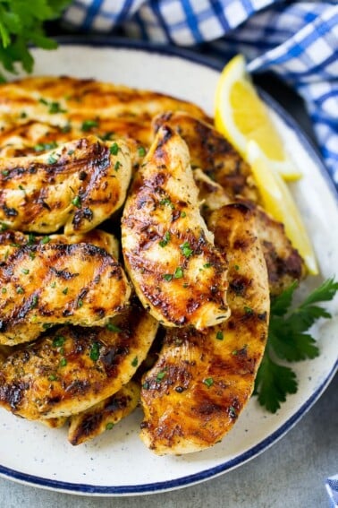 A pile of grilled chicken tenders topped with fresh herbs and garnished with lemon wedges.