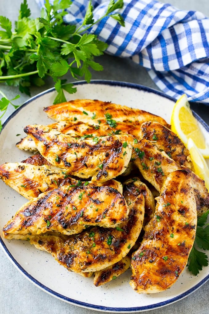 Grilled chicken tenders on a plate garnished with parsley and lemon wedges.