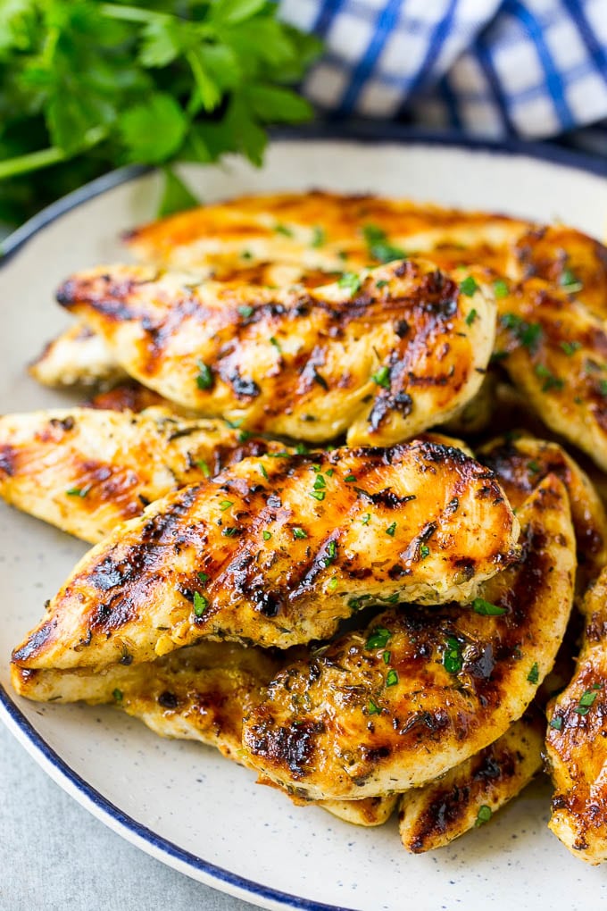 A plate of grilled chicken tenders topped with chopped parsley.