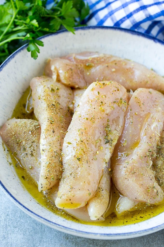 Raw chicken tenders in a marinade of olive oil, garlic, lemon juice and herbs.