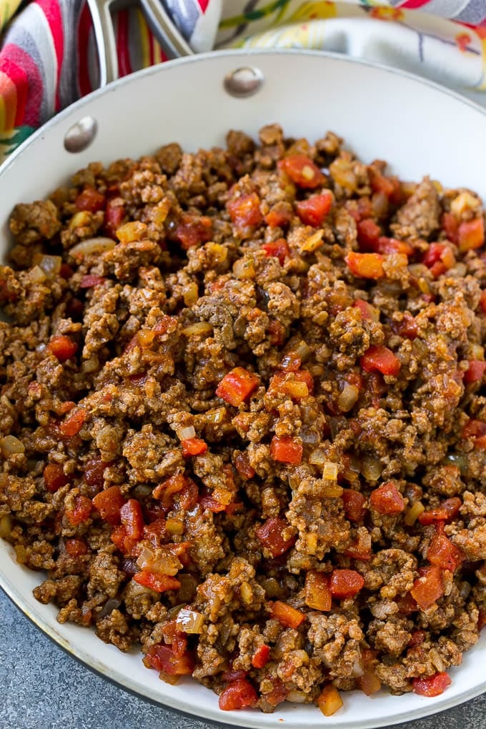 A skillet of ground beef cooked with taco seasoning, onions and tomatoes.