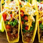 Ground beef tacos in hard taco shells topped with shredded cheese, lettuce, tomato and onion.