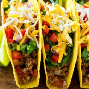 Ground beef tacos in hard taco shells topped with shredded cheese, lettuce, tomato and onion.