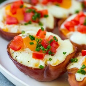 A plate of ham and egg cups topped with diced tomatoes and chives.