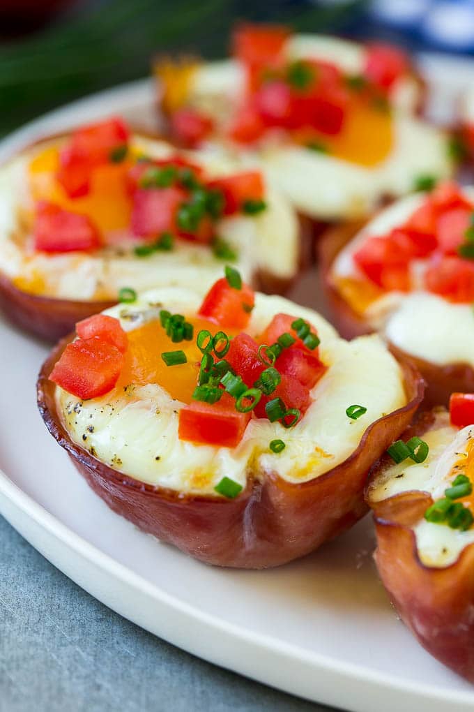 A plate of ham and egg cups topped with diced tomatoes and chives.