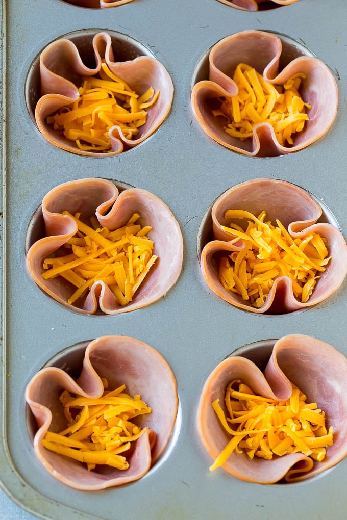 Ham pressed into muffin tins and topped with shredded cheese.