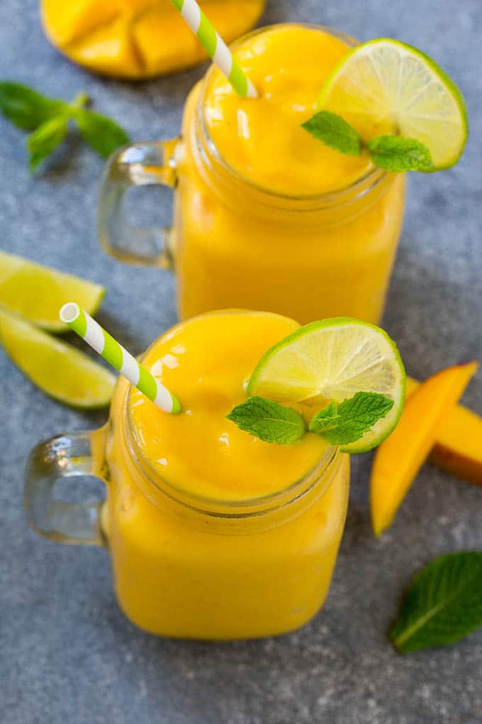 Two jars full of mango smoothie, garnished with lime slices and fresh mint.