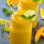 Mango smoothie in a mug topped with a slice of lime and mint sprig.