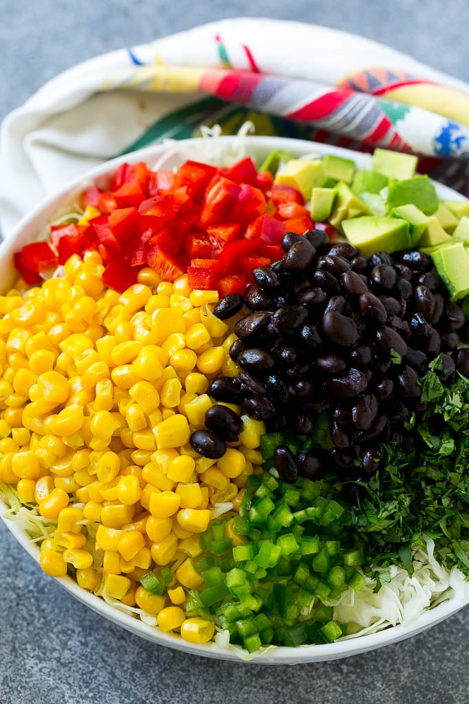 A bowl of shredded cabbage, corn, black beans, red peppers, jalapeno and avocado.