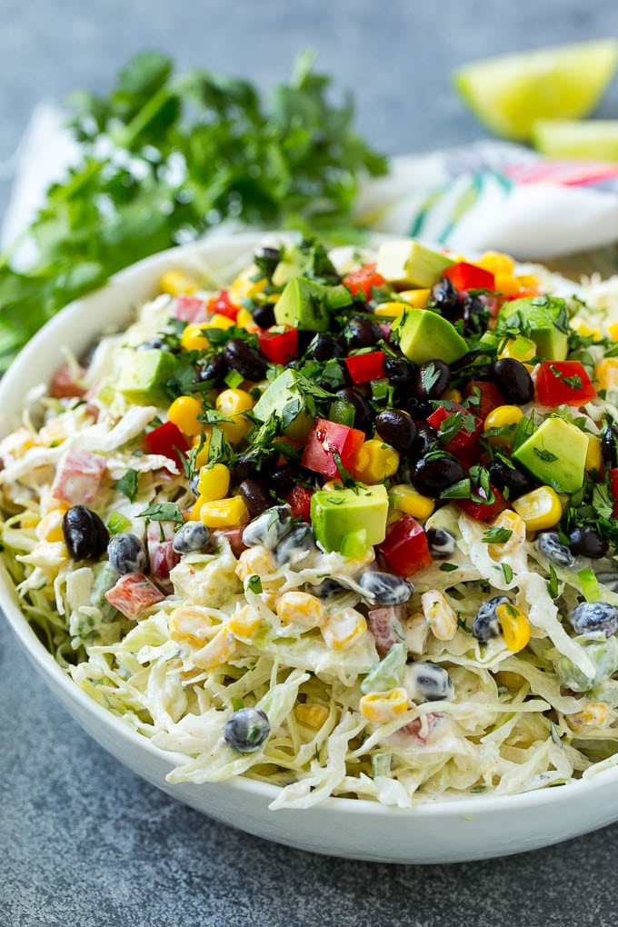 A bowl of Mexican coleslaw topped with black beans, corn, red peppers and avocado.