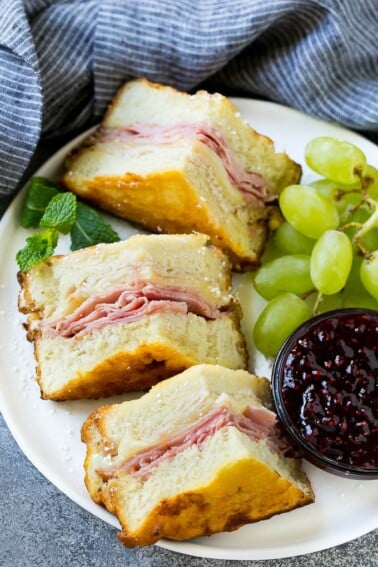 A plate of Monte Cristo sandwich with fresh fruit and raspberry jam for dipping.