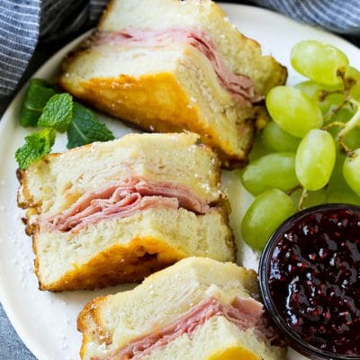 A plate of Monte Cristo sandwich with fresh fruit and raspberry jam for dipping.