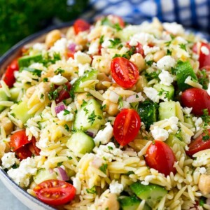 Orzo salad in a serving bowl with tomatoes, cucumbers and chickpeas.