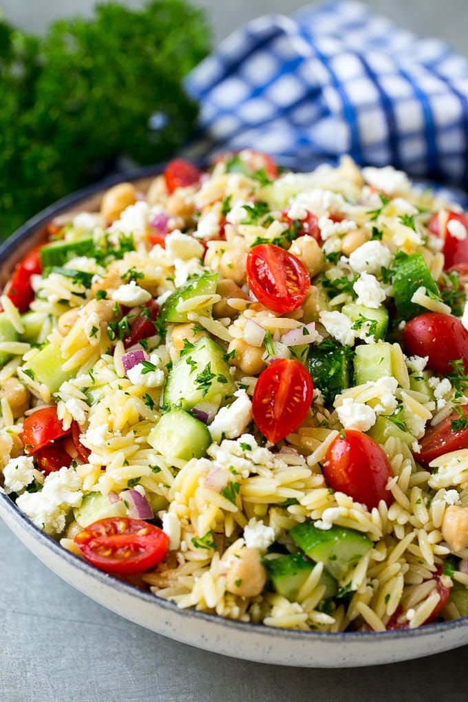 Orzo salad in a serving bowl with tomatoes, cucumbers and chickpeas.