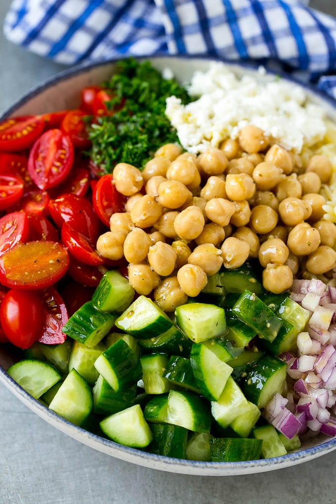 A bowl of orzo pasta, tomatoes, cucumbers, red onions, chickpeas and feta cheese topped with dressing.