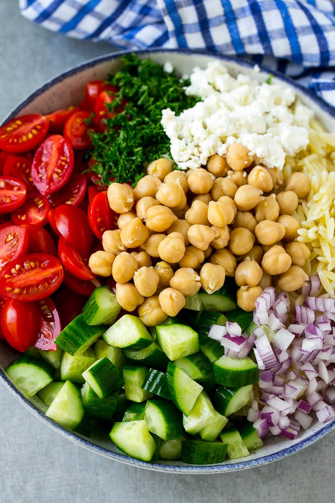 A bowl of orzo pasta, cucumbers, cherry tomatoes, feta cheese, red onions, herbs and chickpeas.