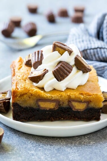 Peanut butter chocolate gooey butter cake topped with whipped cream and chopped peanut butter cups.