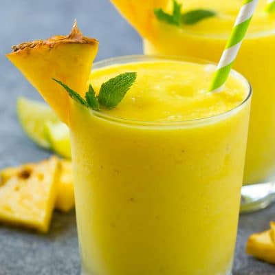 A glass of pineapple smoothie garnished with fresh pineapple and mint.