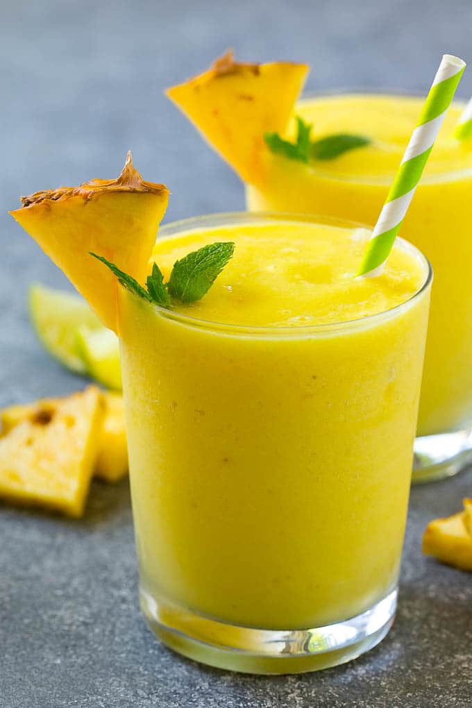 A glass of pineapple smoothie garnished with fresh pineapple and mint.