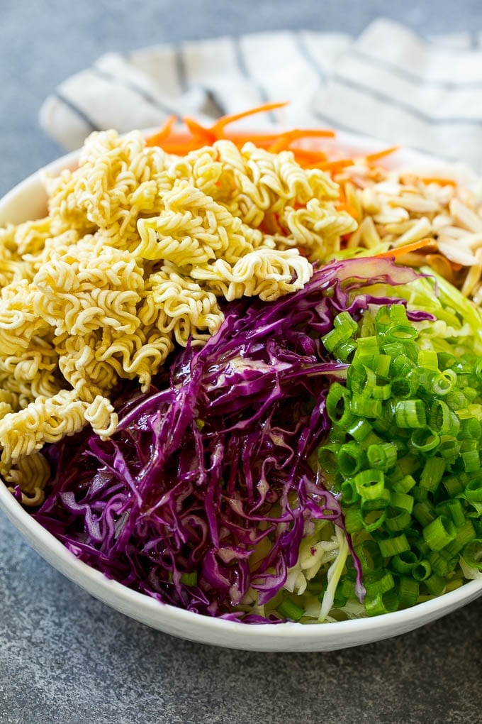 Cabbage, ramen noodles, green onions and carrots in a bowl, drizzled with dressing.