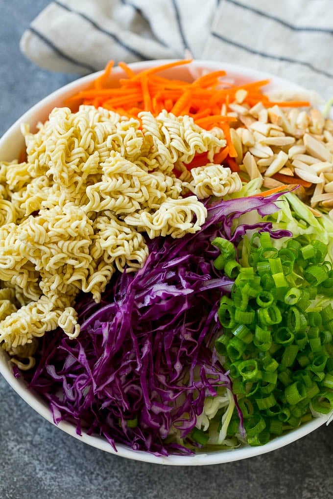 Shredded cabbage, broken up ramen noodles, shredded carrots, almonds and green onions in a bowl.