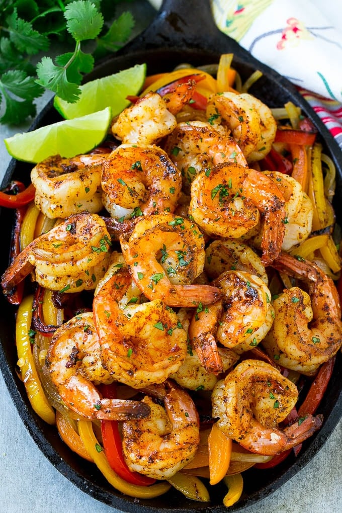 A skillet of shrimp fajitas with peppers, onions, lime wedges and fresh cilantro.