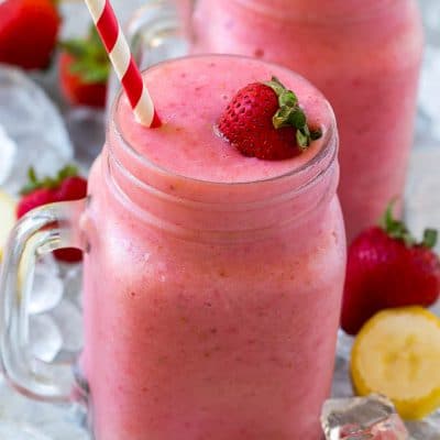 A mason jar mug of strawberry banana smoothie with fresh strawberry on top.