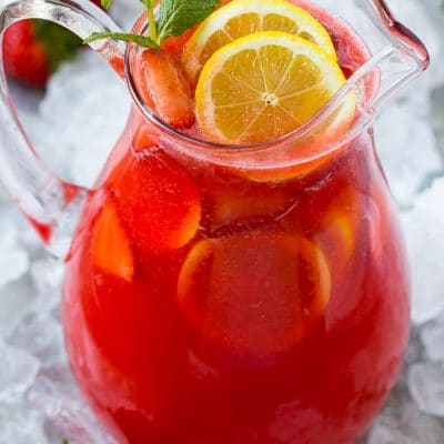 A pitcher of strawberry lemonade garnished with sliced lemons and mint.