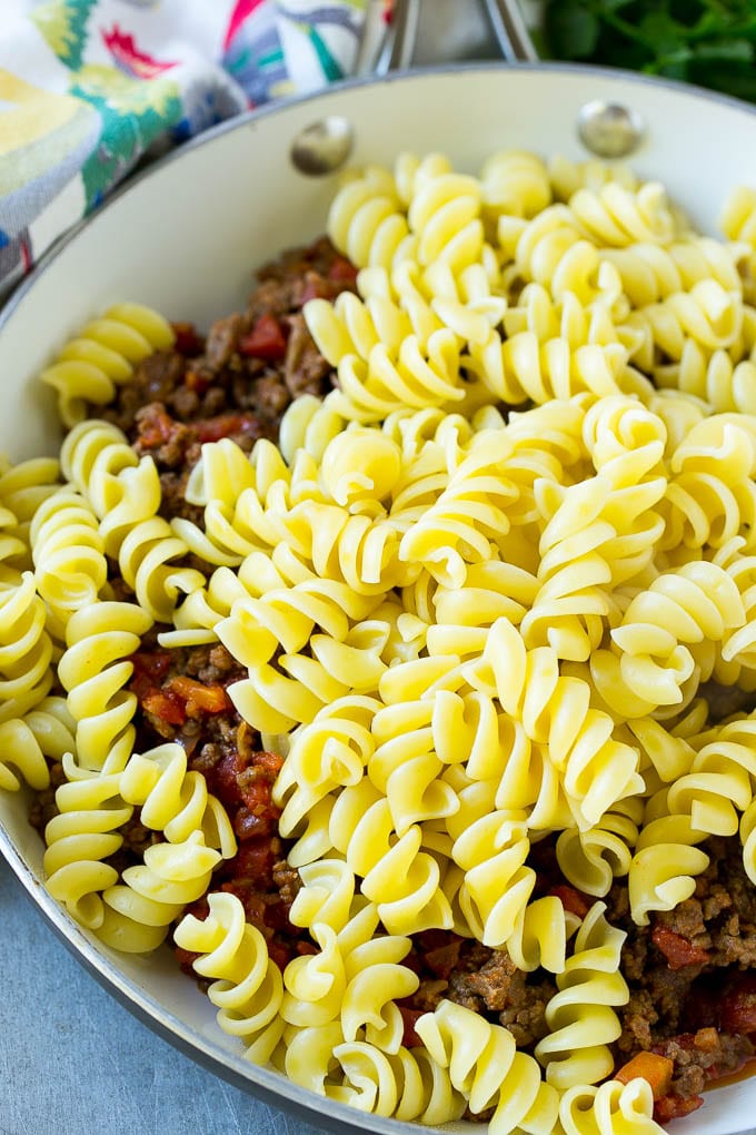 A skillet of cooked ground beef seasoned with tomatoes, and rotini pasta.