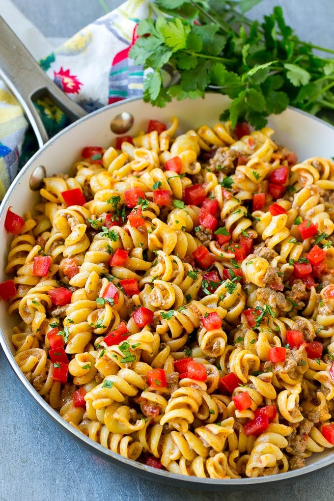 A skillet of taco pasta topped with fresh diced tomatoes and cilantro.