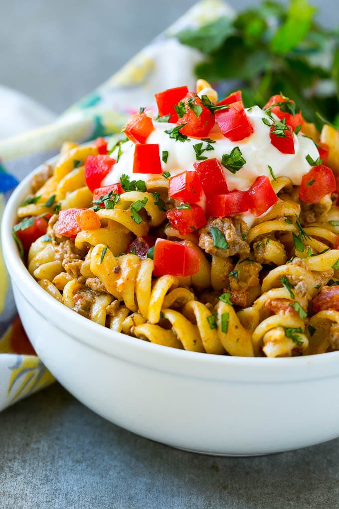 A bowl of taco pasta topped with sour cream, tomatoes and cilantro.