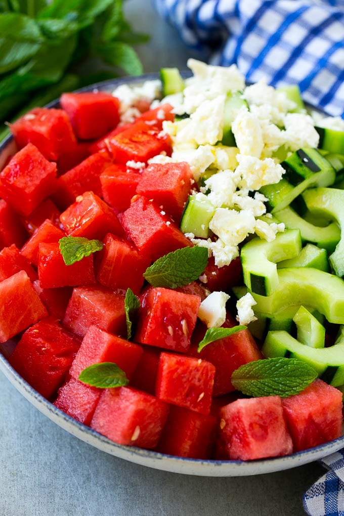 A bowl of watermelon, cucumber, feta cheese and mint leaves drizzled with lime dressing.