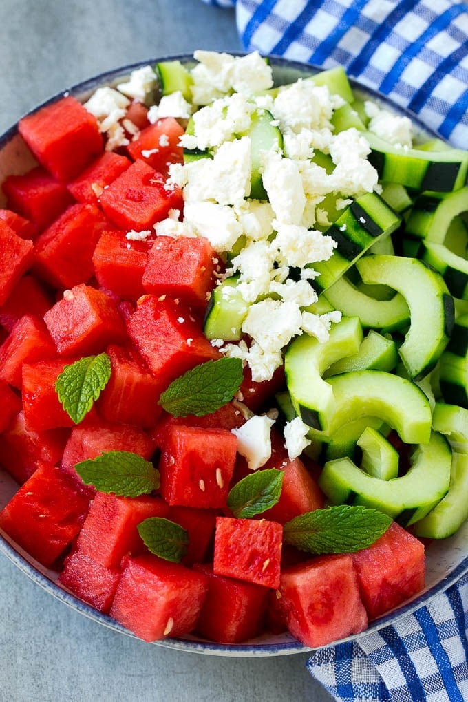 A bowl of cubed watermelon, sliced cucumbers, feta cheese and mint leaves.