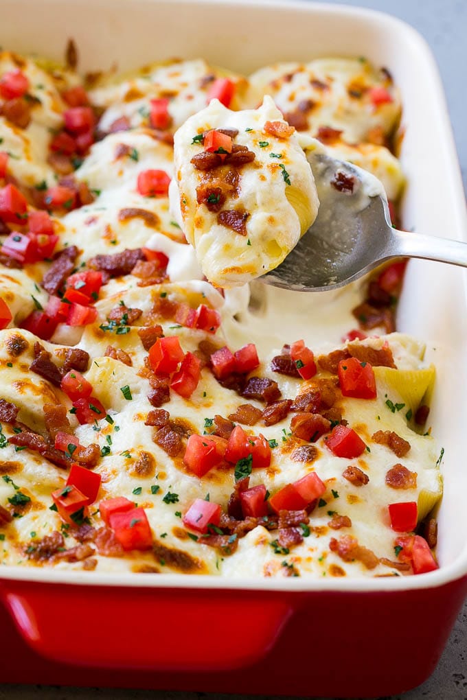 A pan of chicken alfredo stuffed shells with a serving spoon.