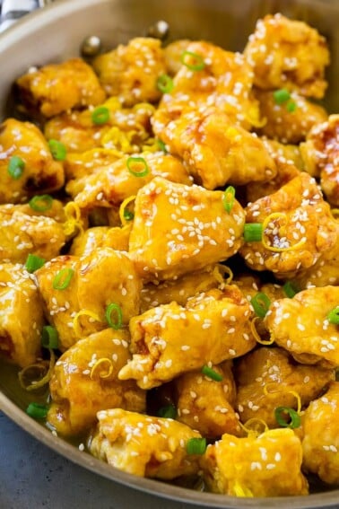 Chinese lemon chicken in a frying pan, garnished with lemon zest, sesame seeds and green onions.