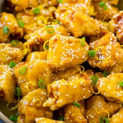 Chinese lemon chicken in a frying pan, garnished with lemon zest, sesame seeds and green onions.