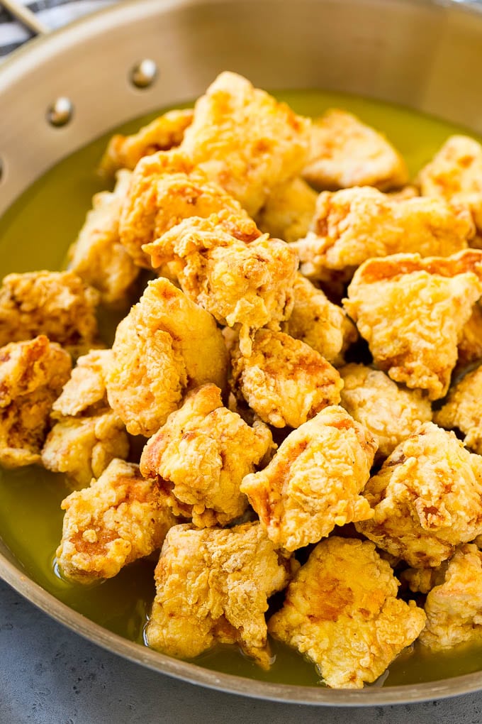 Fried chicken pieces in a pan of lemon sauce.