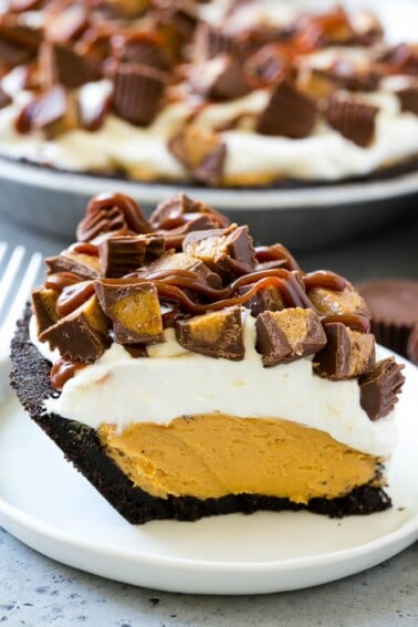 A slice of chocolate peanut butter pie topped with whipped cream, chocolate sauce and peanut butter cups.